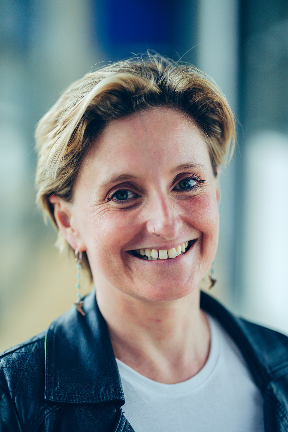 Headshot of Claire: a fifty year old white woman with shoulder-length brown hair, a pierced nose and pierced ears, green eyes, a rosy complexion, a big smile, and her own teeth (so far).