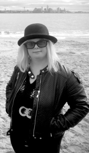 Headshot of Helen Cherry, a white woman with shoulder length blonde hair. She wears a black bowler hat and sunglasses