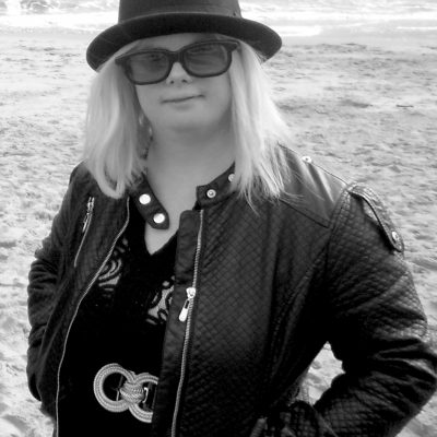 Headshot of Helen Cherry, a white woman with shoulder length blonde hair. She wears a black bowler hat and sunglasses