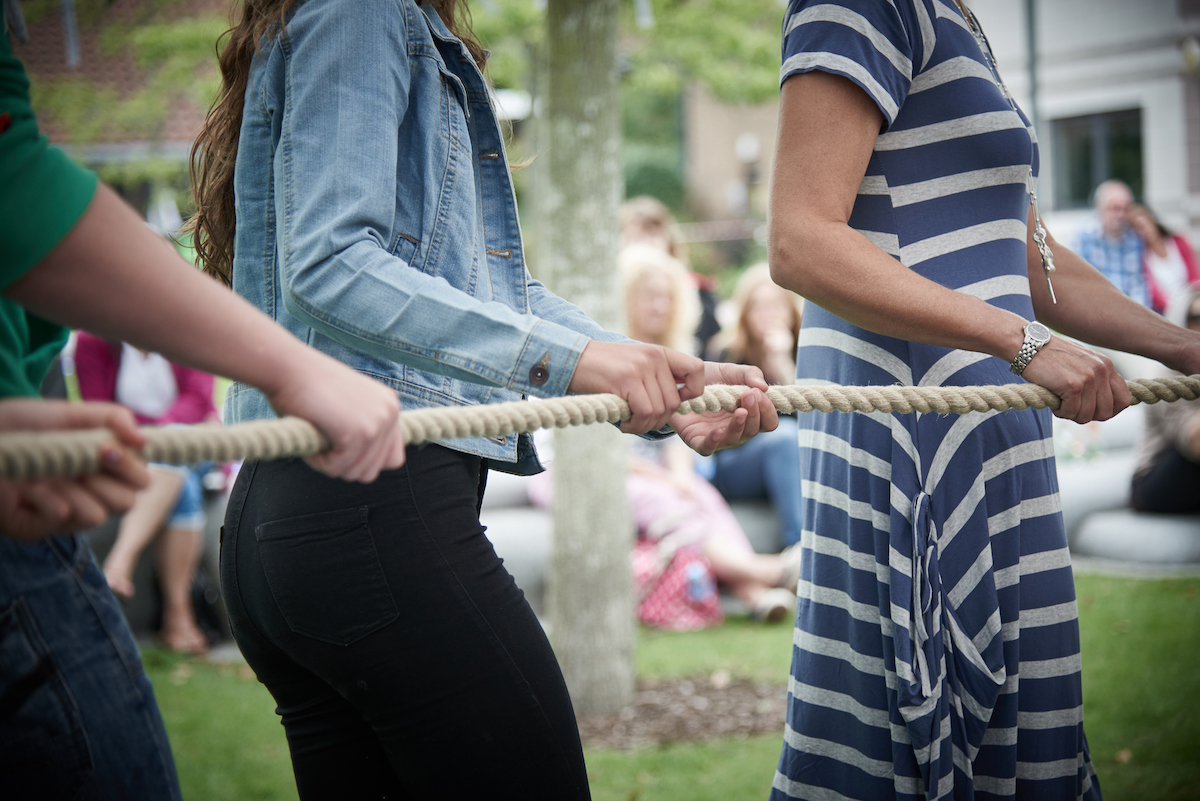 Close up of a group of people in a row, their hands holding a rope.
