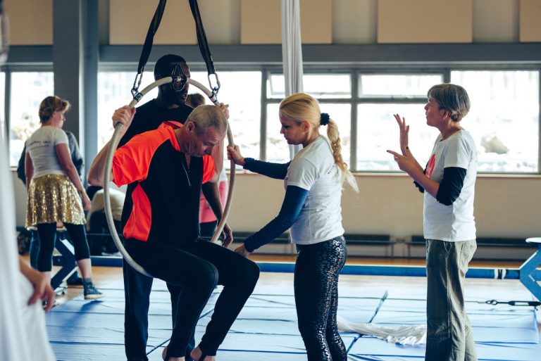 Extraordinary Bodies artists lead a workshop; one artist assists a workshop participant into an aerial hoop. A BSL interpreter communicates with David Ellington.