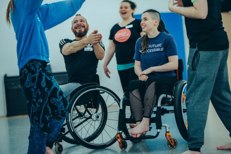 Extraordinary Bodies Young Artists moving around a rehearsal room. One of the young theatre members is a wheelchair user; her tshirt reads 'THE FUTURE IS ACCESSIBLE'