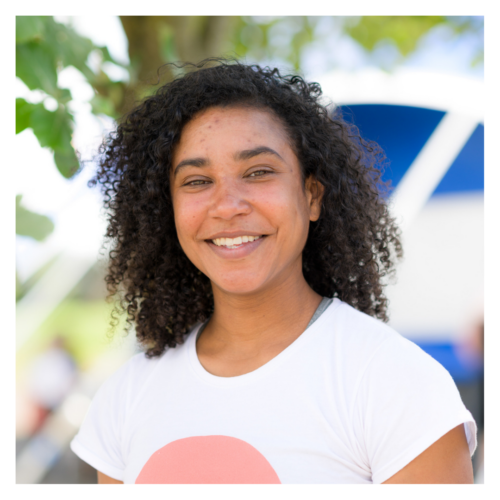 Alfa: a short, slim, mixed-race woman in her thirties with dark short curly hair. She is smiling brightly at the camera.