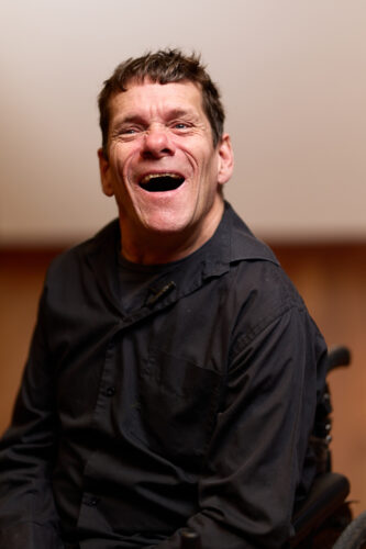 Jamie Beddard, close up and happily laughing in his wheelchair.