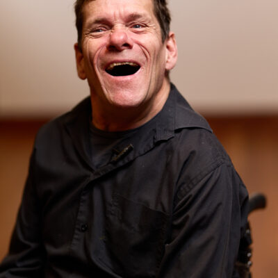 Jamie Beddard, close up and happily laughing in his wheelchair.